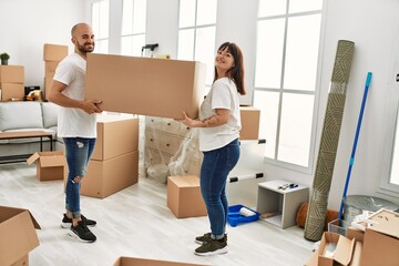 Fototapeta na wymiar Young hispanic couple smiling happy holding big cardboard box at new home.
