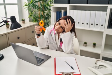 Young hispanic doctor woman holding awareness orange ribbon stressed and frustrated with hand on...