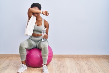 African american woman wearing sportswear sitting on pilates ball smiling cheerful playing peek a boo with hands showing face. surprised and exited