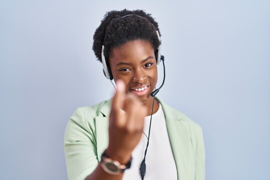 African american woman wearing call center agent headset beckoning come here gesture with hand inviting welcoming happy and smiling