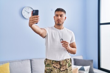 Young hispanic man wearing camouflage army uniform taking selfie at home skeptic and nervous, frowning upset because of problem. negative person.