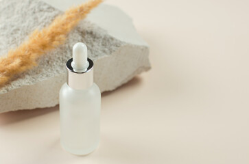 Essential oil or serum and dry pampas herbs on a natural white podium. Frosted bottle with a pipette on a beige background