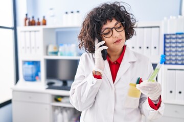 Young beautiful hispanic woman scientist talking on smartphone holding test tube at street