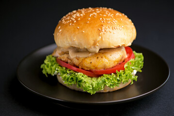 Close-up of a delicious fresh homemade burger with lettuce, cheese, onion and tomato on a rustic wooden board on a dark background