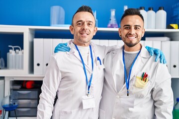 Two men scientists smiling confident hugging each other at laboratory