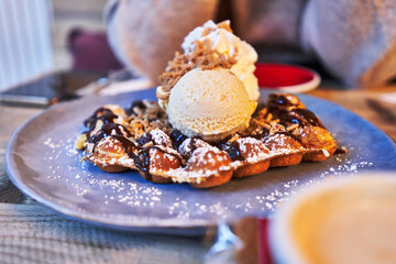  Plate of waffle with chocolate sauce and ice cream on wooden surface