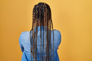African american woman with braids standing over yellow background standing backwards looking away with crossed arms