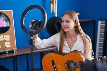 Fototapeta na wymiar Young caucasian woman musician playing classical guitar record by smartphone at music studio