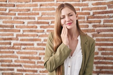 Young caucasian woman standing over bricks wall background touching mouth with hand with painful expression because of toothache or dental illness on teeth. dentist