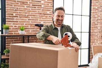 Young caucasian man smiling confident packing cardboard box at new home