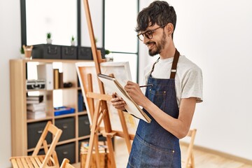 Young hispanic artist man smiling happy drawing at art studio.