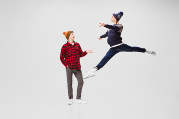 Friends, lovers or rivals. Young men, ballet dancers in warm clothes and hats dancing, jumping isolated on gray background. Music, dance, fashion