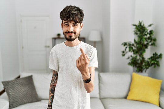 Hispanic man with beard at the living room at home beckoning come here gesture with hand inviting welcoming happy and smiling