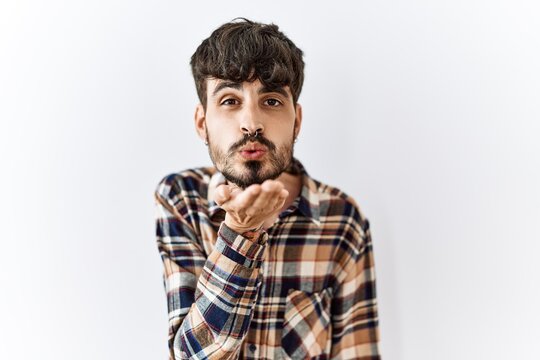 Hispanic man with beard standing over isolated background looking at the camera blowing a kiss with hand on air being lovely and sexy. love expression.