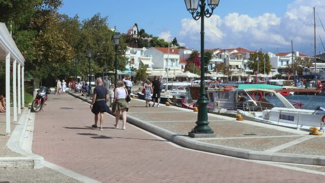Tourists Strolling Around The Pretty Harbour With Fishing Boats On The Greek Island Of Skiathos On A Hot September Day With Blue Sky And White Clouds