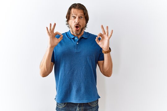 Handsome middle age man standing together over isolated background looking surprised and shocked doing ok approval symbol with fingers. crazy expression