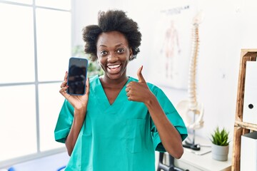 African young physiotherapist woman working at pain recovery clinic showing smartphone screen...