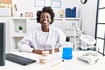 African dentist woman working at medical clinic looking positive and happy standing and smiling with a confident smile showing teeth
