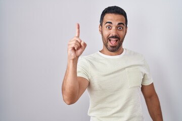 Fototapeta premium Hispanic man with beard standing over isolated background pointing finger up with successful idea. exited and happy. number one.