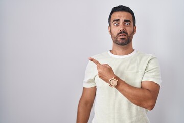 Hispanic man with beard standing over isolated background pointing aside worried and nervous with...