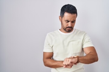 Fototapeta premium Hispanic man with beard standing over isolated background checking the time on wrist watch, relaxed and confident