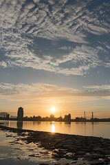 Obraz premium Sunset City Skyline Reflecting on Calm Water Under Dramatic Clouds