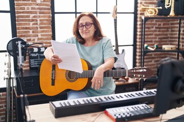 Fototapeta na wymiar Senior woman musician playing classical guitar reading paper at music studio