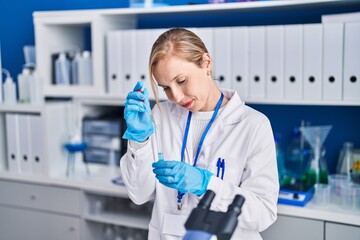 Young blonde woman scientist pouring liquid on test tube at laboratory