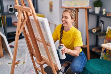 Young blonde woman artist smiling confident using graffiti spray drawing at art studio