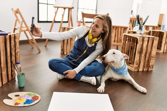 Young caucasian woman make selfie by the smartphone with dog at art studio