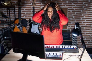 Plus size hispanic woman playing piano at music studio suffering from headache desperate and...