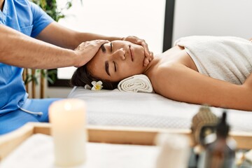 Obraz na płótnie Canvas Latin man and woman wearing physiotherapy uniform having rehab session massaging head at beauty center