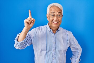 Hispanic senior man wearing glasses pointing finger up with successful idea. exited and happy. number one.