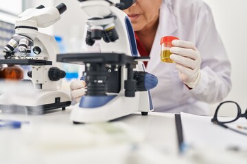 Middle age hispanic woman wearing scientist uniform analysing urine test using microscope at laboratory
