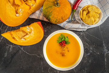 Autumn pumpkin cream soup with pumpkin spices. Delicious and bright vegetarian dish with foodstyling of fresh parsley with hot pepper and seasonings on a dark background. Menu concept, copy space