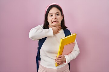 Woman with down syndrome wearing student backpack and holding books cutting throat with hand as knife, threaten aggression with furious violence
