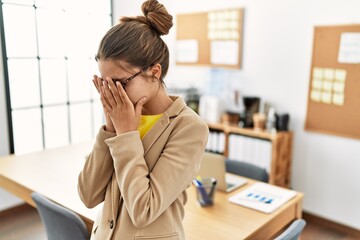 Young brunette teenager wearing business style at office with sad expression covering face with...