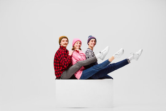 Happy, cheerful men and girl in warm clothes and hat sitting, having fun isolated on gray background. Love, relationships, family, art
