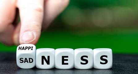 Hand turns dice and changes the word sadness to happiness.