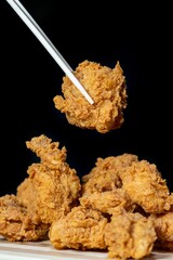 Set of chop sticks picking up fried chicken against a dark background