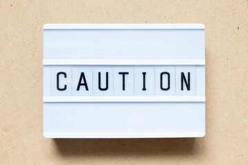 Lightbox with word caution on wood background