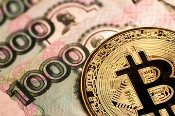 close-up of a golden bitcoin coin against the background of a banknote of 1000 Russian rubles