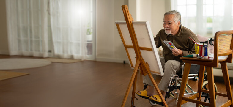 panoramic of disabled artist senior man drawing sitting on wheel chair at home.small business,entrepreneurship and Home hobby after retirement.Disabled Elderly male in wheelchair at art studio