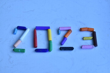 Numerals 2023 from multi-colored pastel crayons on a light background.