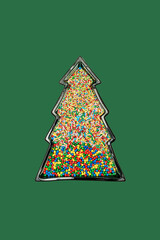Christmas tree shaped frame filled with many colorful candy sprinkles on green background with copy space. Creative New Year wallpaper idea. Flat lay lay out party theme.