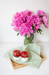 A beautiful bouquet of pink peonies in a vase on a white table stands along with a heart-shaped strawberry dessert. St. Valentine's Day, 8 March.