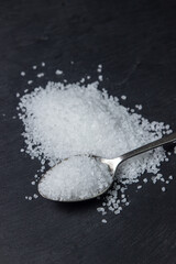 Coarse rock sea salt on a black background.Spoon full of coarse salt