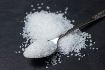 Coarse rock sea salt on a black background.Spoon full of coarse salt