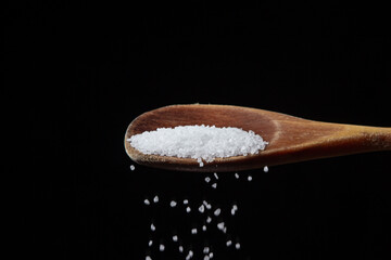 Large rock sea salt on a black background. Salt pouring from a wooden spoon