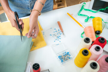 Top view of a young woman's tailor using fabric scissors to work on designing a new collection by hand. Show lots of devices on your desk.